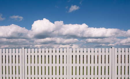 Horizontal front view of a white wooden fence on front of a blue sky with cloudsの写真素材