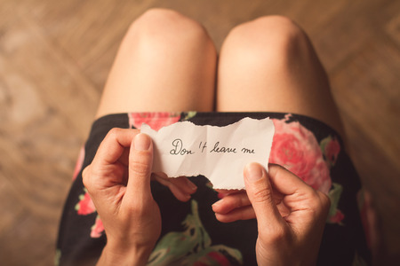 Top view of woman in dark dress holding a paper message with the text do not leave meの写真素材