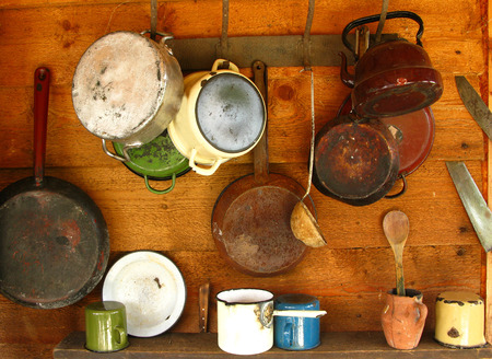 Scratched and damaged old frying pans and cooking pots hanging on a wooden wallの写真素材