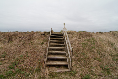 Front view of a damaged old staircase over a grass hill with clouds in the backgroundの写真素材