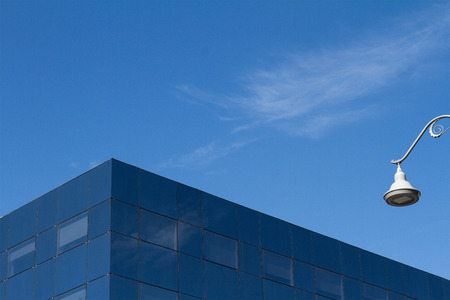 Minimalist photo of a glass office city building detail against a blue sky and a white street lightの写真素材