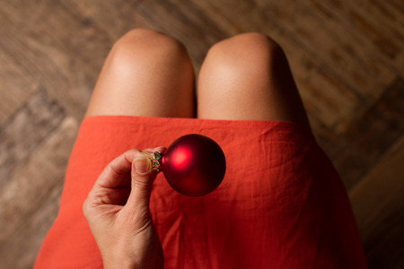 Top view of woman with red dress holding one red Christmas globe above her kneesの写真素材