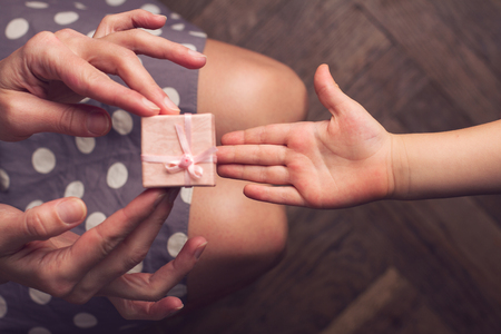 Top view of hands of woman giving a small pink gift box to her kid with open handの写真素材