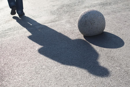 shadow of a man on the street pavement passing by a round decorative sidewalk stoneの写真素材