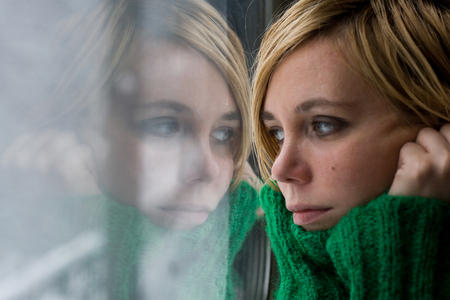 Portrait of a beautiful blonde woman with green warm sweater reflected in a glass window looking...