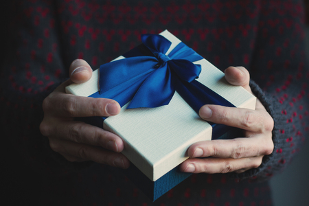 front view close up of a man with black sweater holding a gift with blue ribbonの写真素材