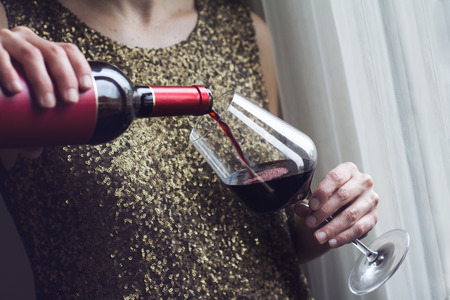 Horizontal close up of Caucasian retro woman in gold sequin vintage dress pouring red wine into a...