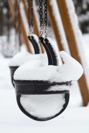 Vertical perspective view of black plastic child swings in the park covered in snowの写真素材