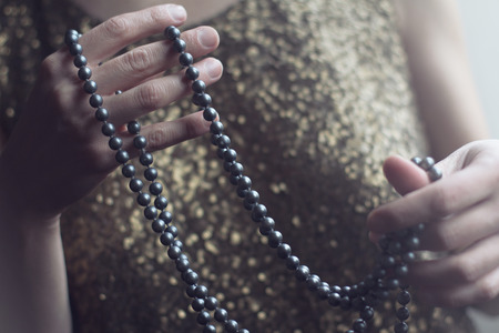 close up of a retro woman in gold sequin vintage dress holding a necklace of black pearls with her handsの写真素材