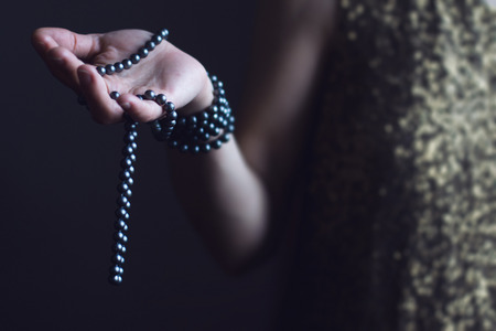 close up of a Caucasian retro woman in gold sequin vintage dress holding a necklace of black pearls...