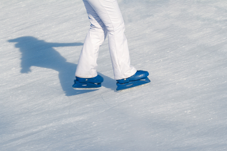 Side view close up of woman in white ski pants and blue iceskates skating on ice rink in wintertimeの写真素材