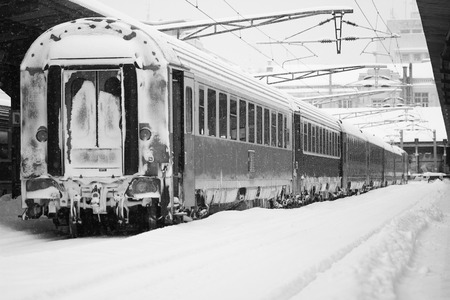 Rear view of the back of a passenger train covered in blizzard snow stopped in railway station, winter timeの写真素材