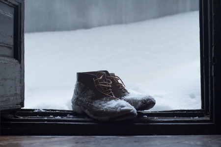 front view of a pair of vintage brown leather shoes by the house wooden open door entrance covered in snow in winter timeの写真素材