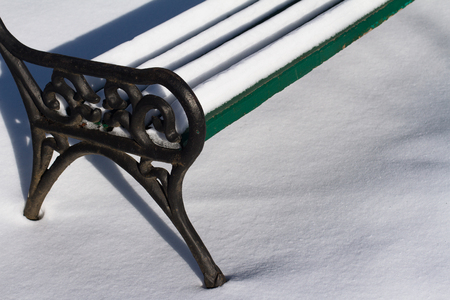 horizontal closeup detail of a wooden park bench with metallic frame covered in snow
