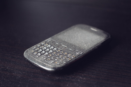 side view close up of old black smartphone mobile with qwerty keyboard covered in dust left on a black wooden shelf, selective focusの写真素材