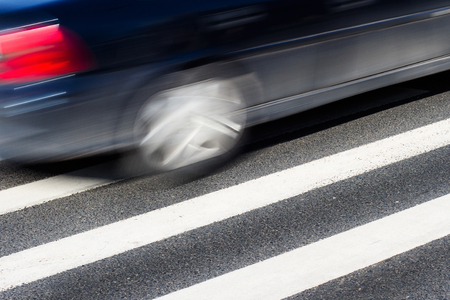 Horizontal side view of a black car with motion blur speeding over a pedestrian crossingの写真素材