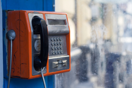 Vertical side view of damaged orange public phone with near a dirty window with selective focusの写真素材