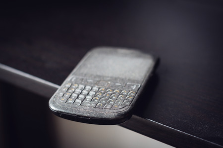 side view close up of old black smartphone mobile with qwerty keyboard covered in dust left on a...