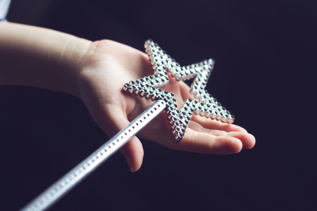horizontal side view of a child hand holding a star shaped silver magic wand on dark background selective focusの写真素材
