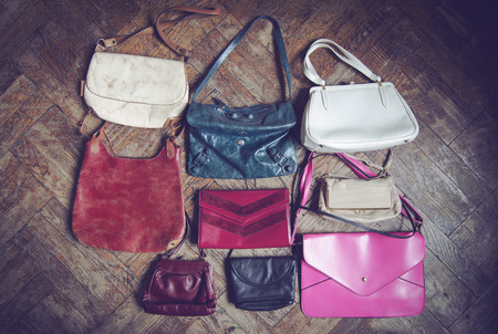 vertical front view of many female hand bags in different shapes sizes and colors hanging on a white wallの写真素材