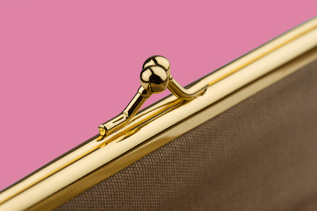 macro detail of closed female cream colored vintage wallet with golden metal enclosure on pink backgroundの写真素材