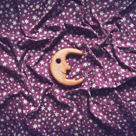 square top view concept wrinkled background texture of purple textile table cloth with white stars and wooden toy moon smiling in the centerの写真素材
