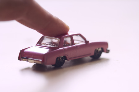 front view closeup of finger pushing forward a little miniature pink toy car on light backgroundの写真素材