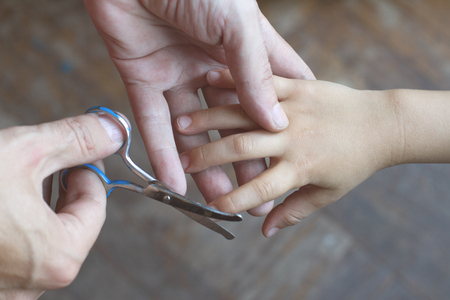 closeup of father hands cutting the dirty nails of his daughter with small safety scissorsの写真素材