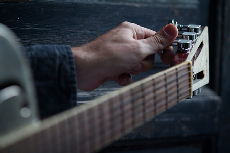 Caucasian male hand tuning an acoustic guitar on black dark wooden background with selective focusの写真素材