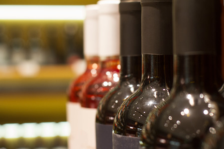 perspective view closeup of row red and rose wine bottles in supermarket shelf with selective focusの写真素材