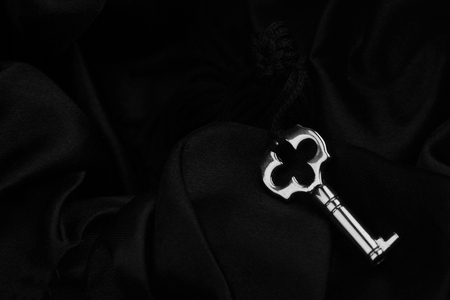 top view of small silver vintage lock key with fabric thread on black silk backgroundの写真素材