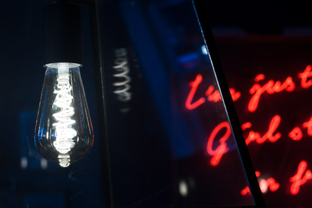 Edison lightbulb with selective focus and red neon letters in the background