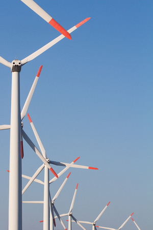 vertical front view of row white eolian wind turbines in a energy farm against a clear blue sky with copyspaceの写真素材