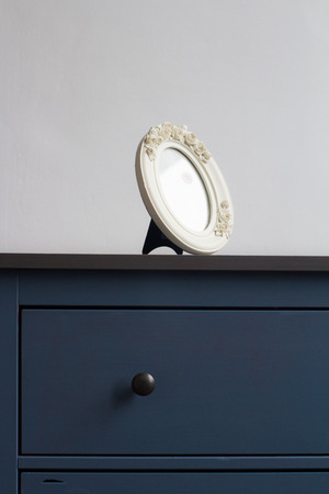 vertical front view detail of white round picture frame on blue vintage wooden chest of drawers with...