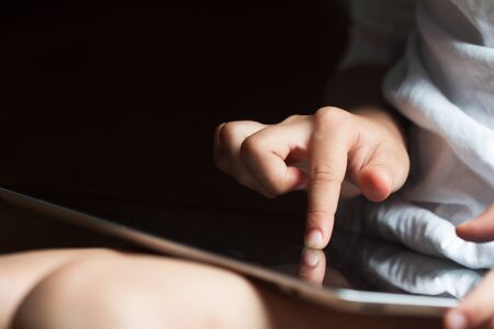 closeup front view of Caucasian child hand touching the screen of a tablet computer in daylightの写真素材