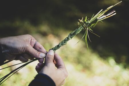 closeup of Caucasian woman hands knitting a green grass traditional diadem garland with knotsの写真素材