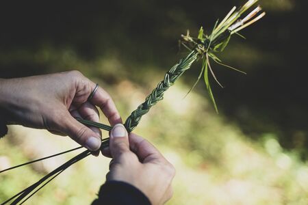 closeup of Caucasian woman hands knitting a green grass traditional diadem garland with knotsの写真素材