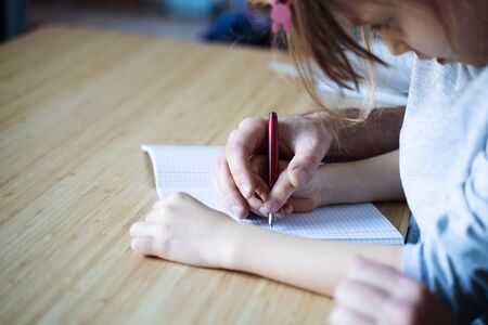 top view of Caucasian adult father helping his child daughter doing the math homework on notebook wooden desk backgroundの写真素材