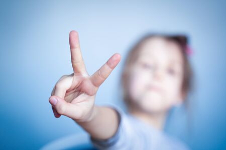 front view closeup with shallow depth of field little girl showing the victory finger symbol with...