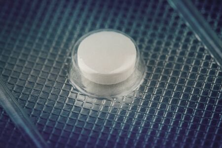 macro closeup of one medical white round pill protected in plastic capsule on silver pharmaceutical packaging blisterの写真素材