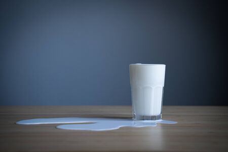 Closeup of glass bottle in a puddle of spilled milk on light colored wood