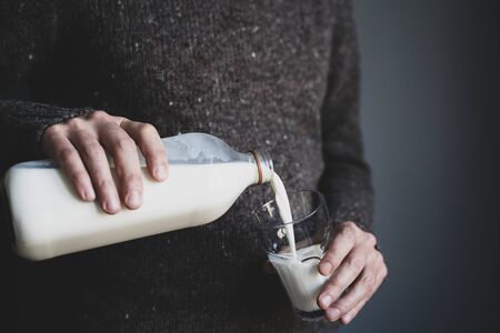 Closeup of young Caucasian man hands in dark wool sweater pouring milk from bottle into a glassの写真素材