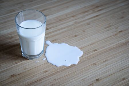 top view closeup of glass bottle in a puddle of spilled milk on light colored wood table background in natural lighting の写真素材