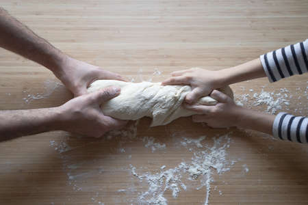 side view close up portrait of Caucasian child hands working the dough at home with his father on a...