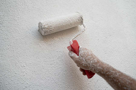 front view closeup of Caucasian male hand full of dirt painting an exterior wall and renovating with white color paint rollerの写真素材