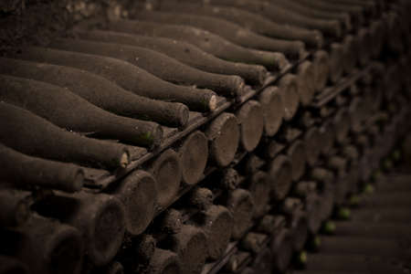perspective view closeup of stacked aged wine bottles ancient collection covered with soft black mold and spiderweb in vintage wine cellarの写真素材