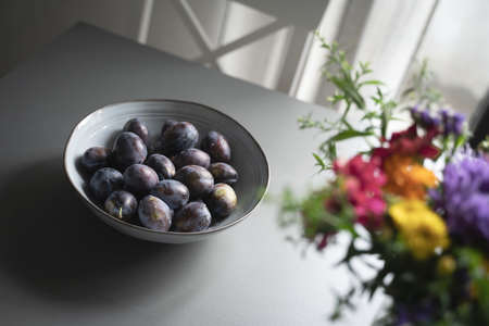 perspective top view of fresh ripe plum fruits in vintage elegant grey bowl on table indoor...