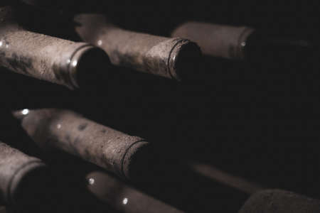 perspective view closeup of stacked aged wine bottles ancient collection covered with soft black...