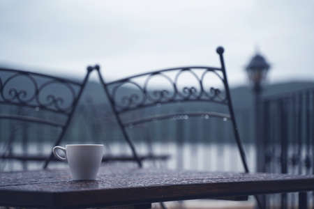 closeup detail of white small espresso coffee cup on wooden table with rain drops on rainy outdoor restaurant terraceの写真素材