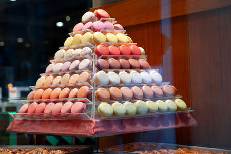 side view closeup of colorful assorted macarons cakes arranged in pyramid shape in candy store windowの写真素材